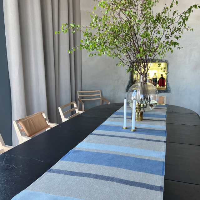 Löpare i linne i randigt med olika färger av blått med växter och ljus som står på löparen